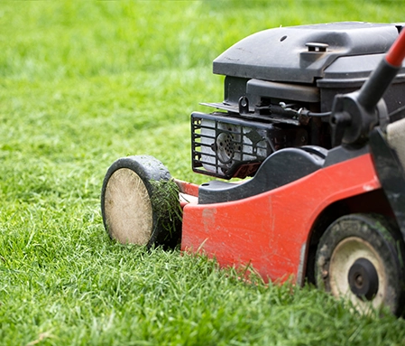 A red lawnmower cuts grass on a large lot.
