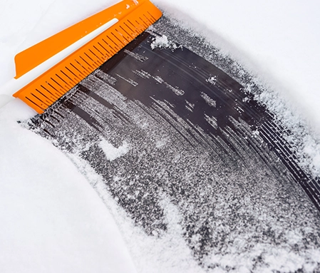 An orange brush removes snow and ice from a windshield.