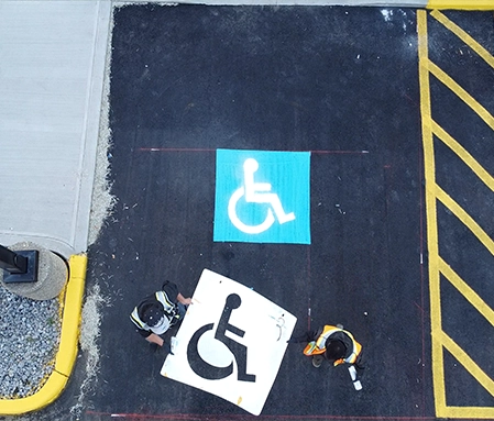 Two Naco employees carry a disabled parking stencil after having just freshly painted the sign in a parking spot.