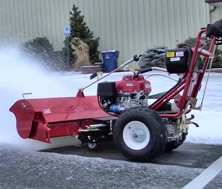 A red snow blower shoots snow off to the side while clearing a parking lot.