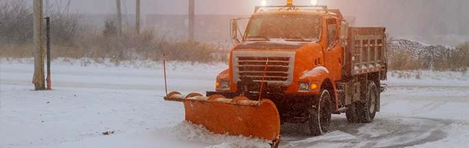 An orange snow plow clears snow from a parking lot.