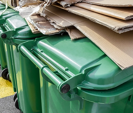Folded cardboard boxes sit atop green recylcing bins.