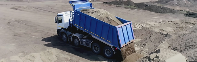 A blue dumptruck dumps sand into a large file.
