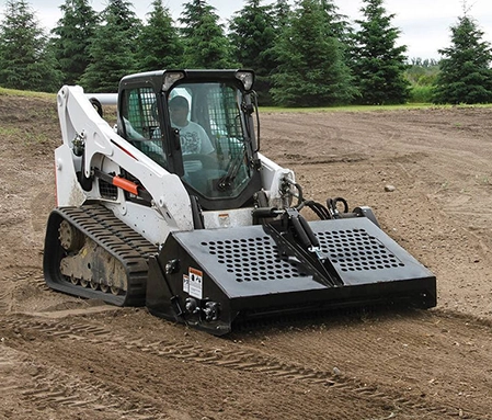 A white skid steer with a landscape rake flattens dirt in a field.