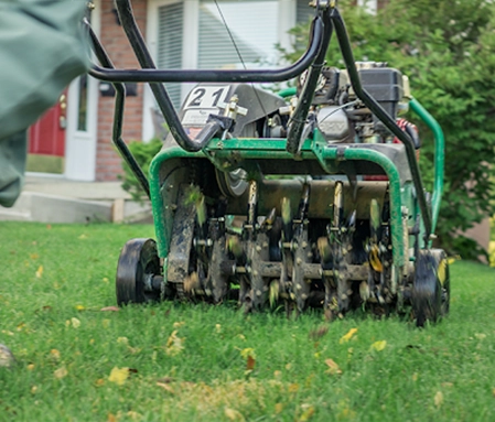 A green lawnmower as it cuts through the lawn of a residential property.
