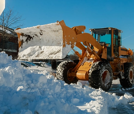 A large orange plow pushes snow into a pile while clearing a parking lot.