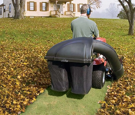 A Naco Commercial Property Solutions team member drives a lawn mower while sucking up leaves scattered around a residential property.